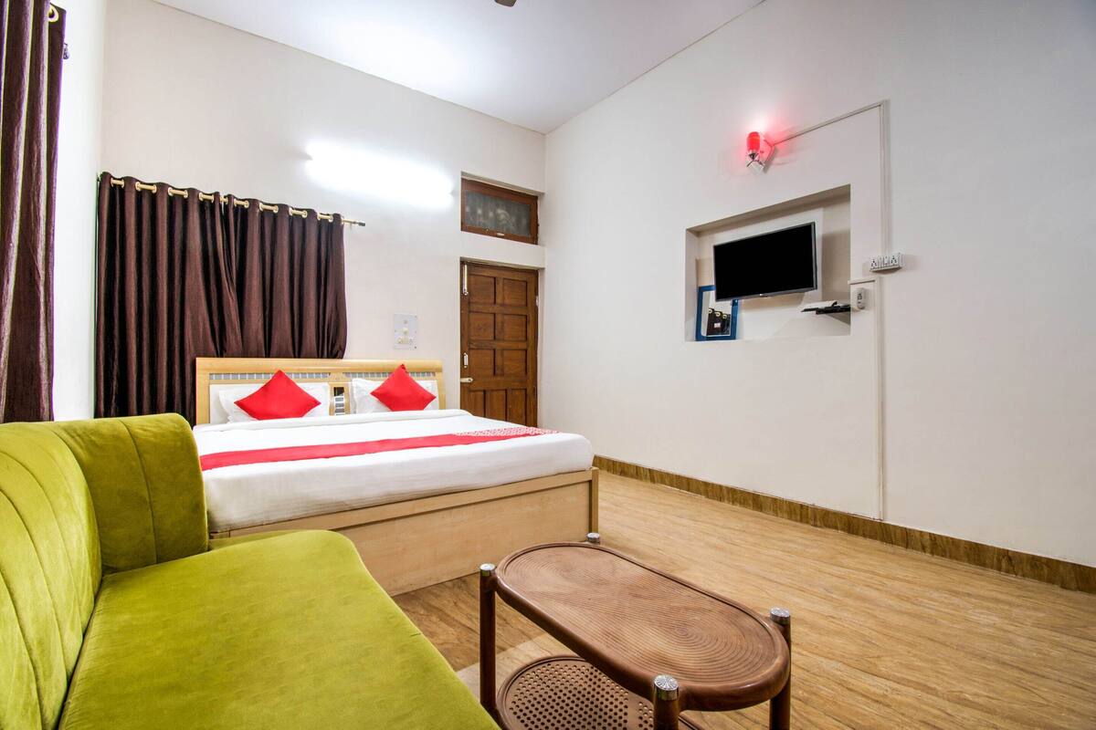 Ein Hotelzimmer mit einem Bett, einem an der Wand befestigten Fernseher, einer Holztür und einem mit Vorhängen versehenen Fenster.