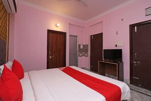 Una habitación de hotel con una cama, almohadas rojas, un televisor sobre un mueble y una puerta.
