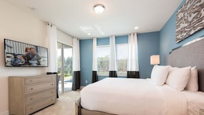 A bedroom with a large bed, a dresser, a TV mounted on the wall, and a window with curtains. - Diamond Villa (Kissimmee)