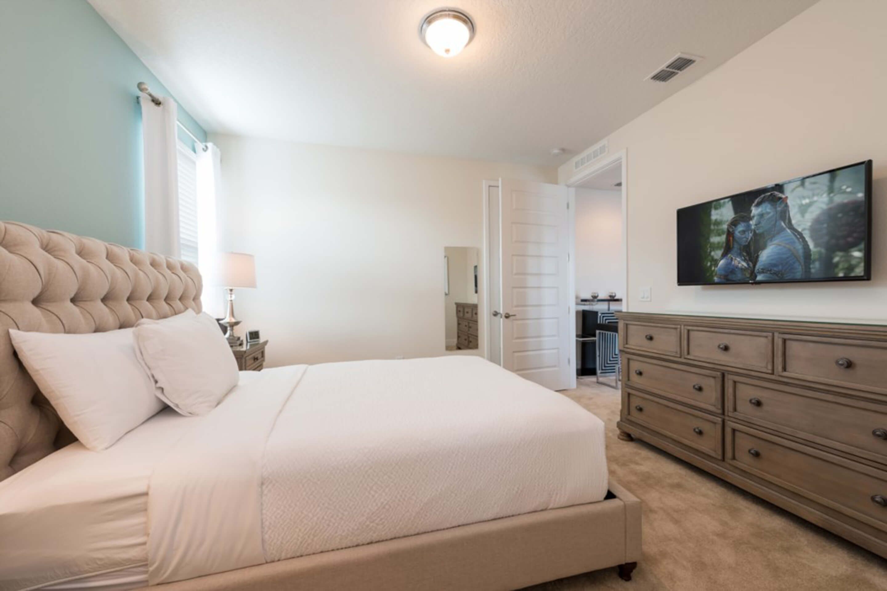 A bedroom with a large bed, a dresser, and a television on the wall.