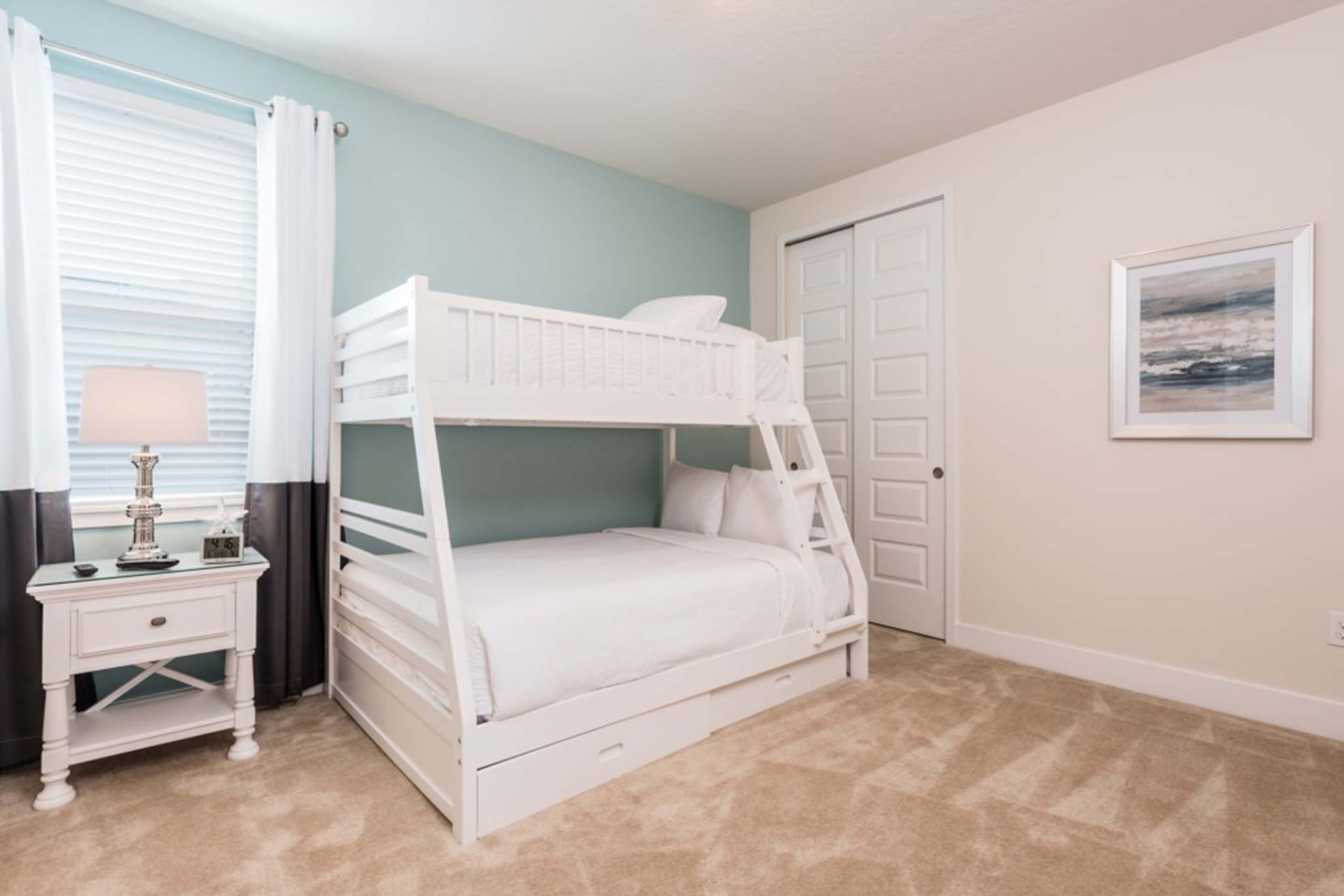 A bunk bed in a room with a light blue wall, a white door, and a framed picture on the wall.