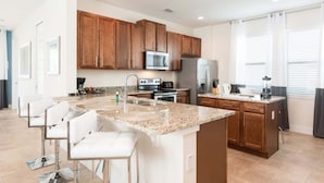 A modern kitchen with granite countertops, stainless steel appliances, and wooden cabinets. - Diamond Villa (Kissimmee)