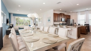 A modern kitchen with a central island, white cabinetry, and a dining area with a glass table and white chairs. - Diamond Villa (Kissimmee)