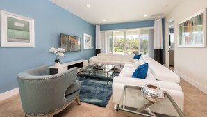 A modern living room with a blue accent wall, a white sofa, a glass coffee table, and a decorative vase. - Diamond Villa (Kissimmee)