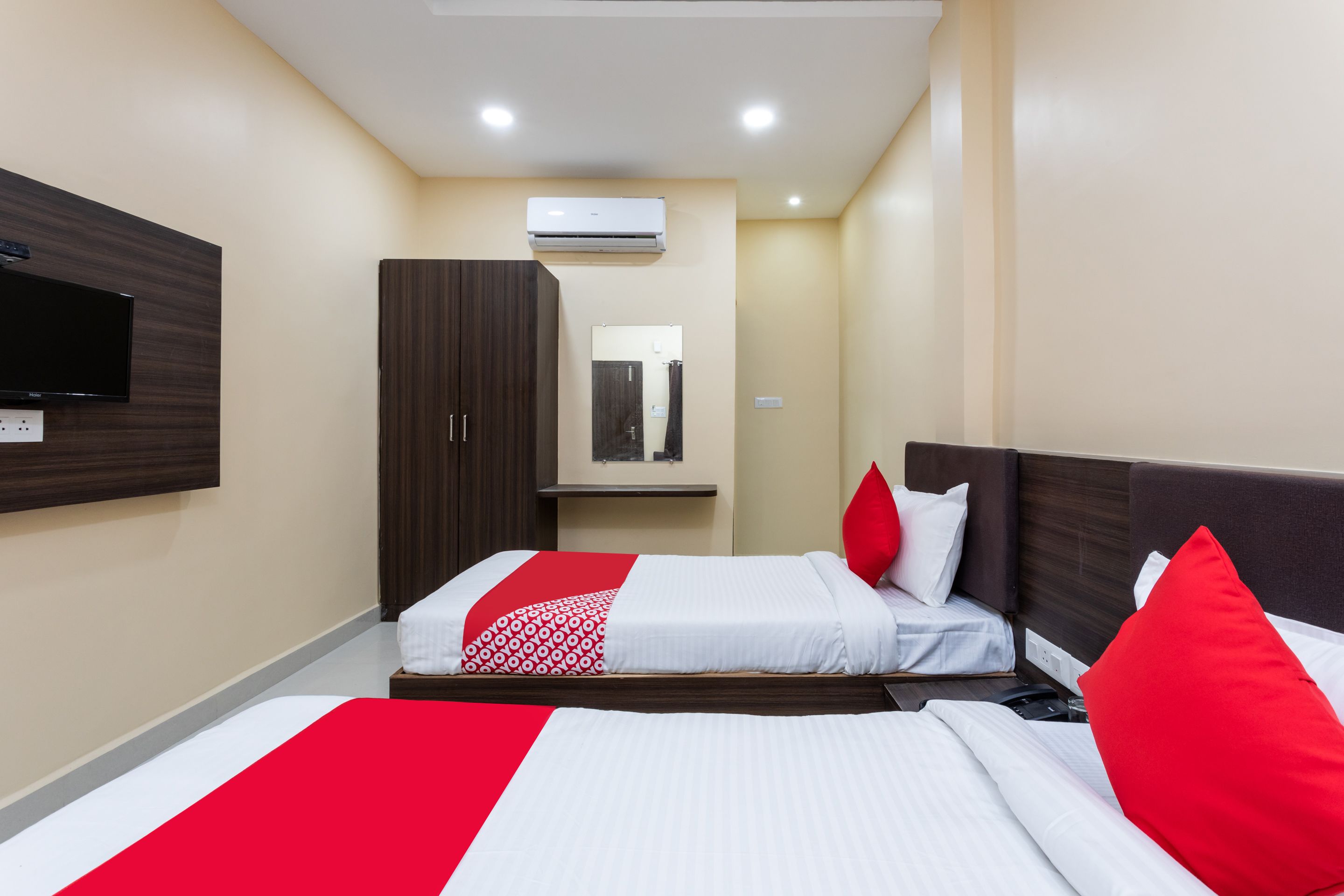 A hotel room with two beds, a TV, an air conditioner, and a mirror.