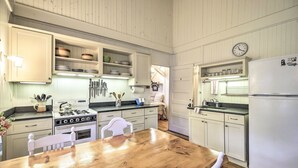 Una cocina con armarios blancos, una mesa de madera y un refrigerador blanco.