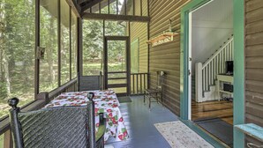 Una cabaña de madera con un porche cubierto, una mesa de comedor con mantel floral y una escalera que sube a un nivel superior.
