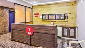A reception area with a wooden reception desk, a blue door, and framed artwork on the wall. - OYO 29878 Sri Abirami Inn (Puducherry)