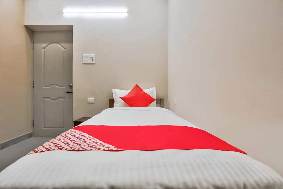 A hotel room with a bed, a red and white bedspread, a white pillow, and a grey door.