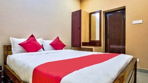 A neatly made bed with white and red bedding, a wooden headboard, and two doors in the background. - OYO 29878 Sri Abirami Inn (Puducherry)