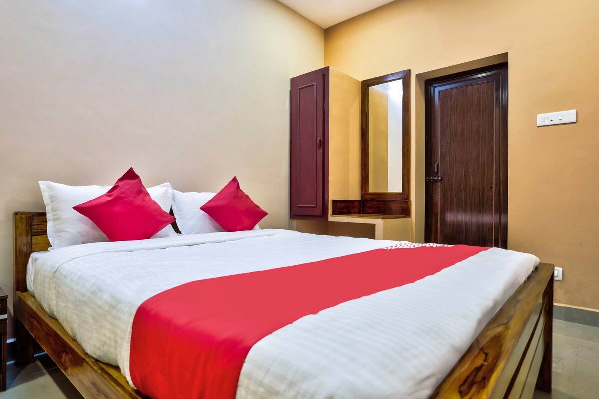 A neatly made bed with white and red bedding, a wooden headboard, and two doors in the background.