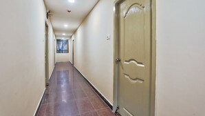 A long, narrow hallway with cream-colored walls and a tiled floor. - OYO 29878 Sri Abirami Inn (Puducherry)