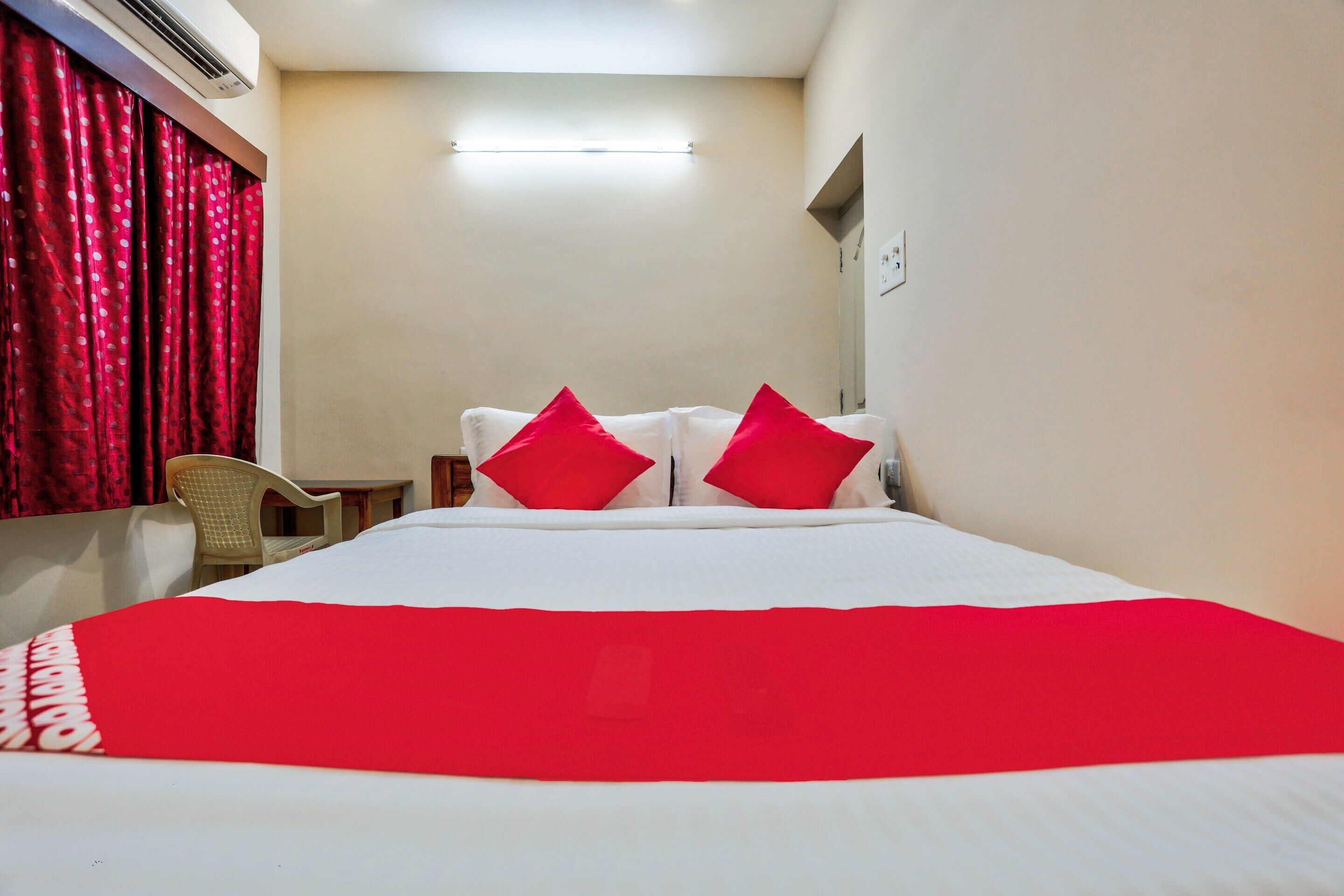 A hotel room with a bed, red curtains, a chair, and a flat-screen TV.