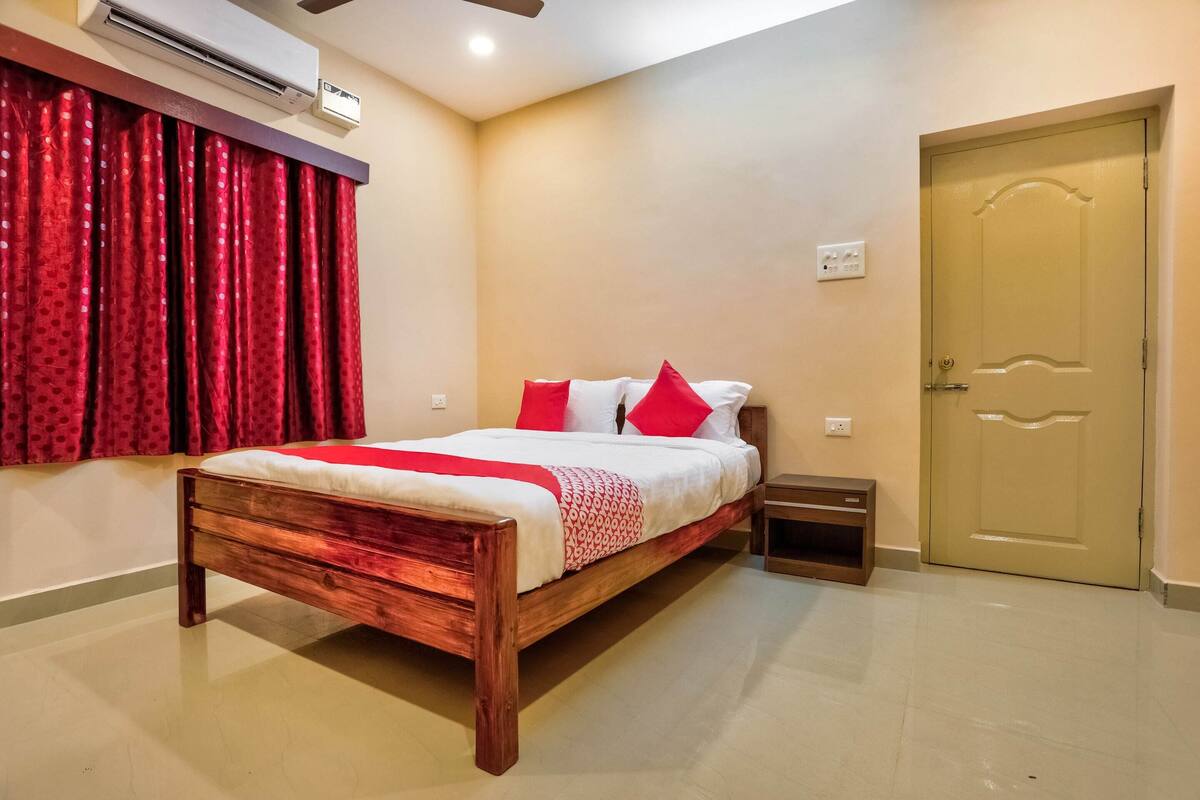 A bedroom with a wooden bed, red curtains, a beige wall, a door, and a small bedside table.