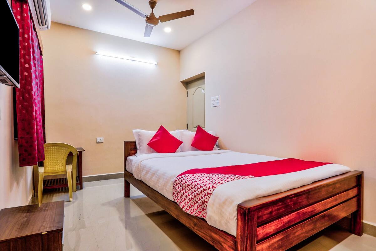 A bedroom with a wooden bed, red and white bedding, a ceiling fan, and a small table.