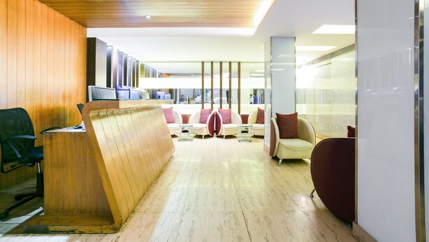Un hall d’entrée moderne avec un comptoir d’accueil en bois, un espace détente avec des canapés et un mur de verre orné de motifs textuels.