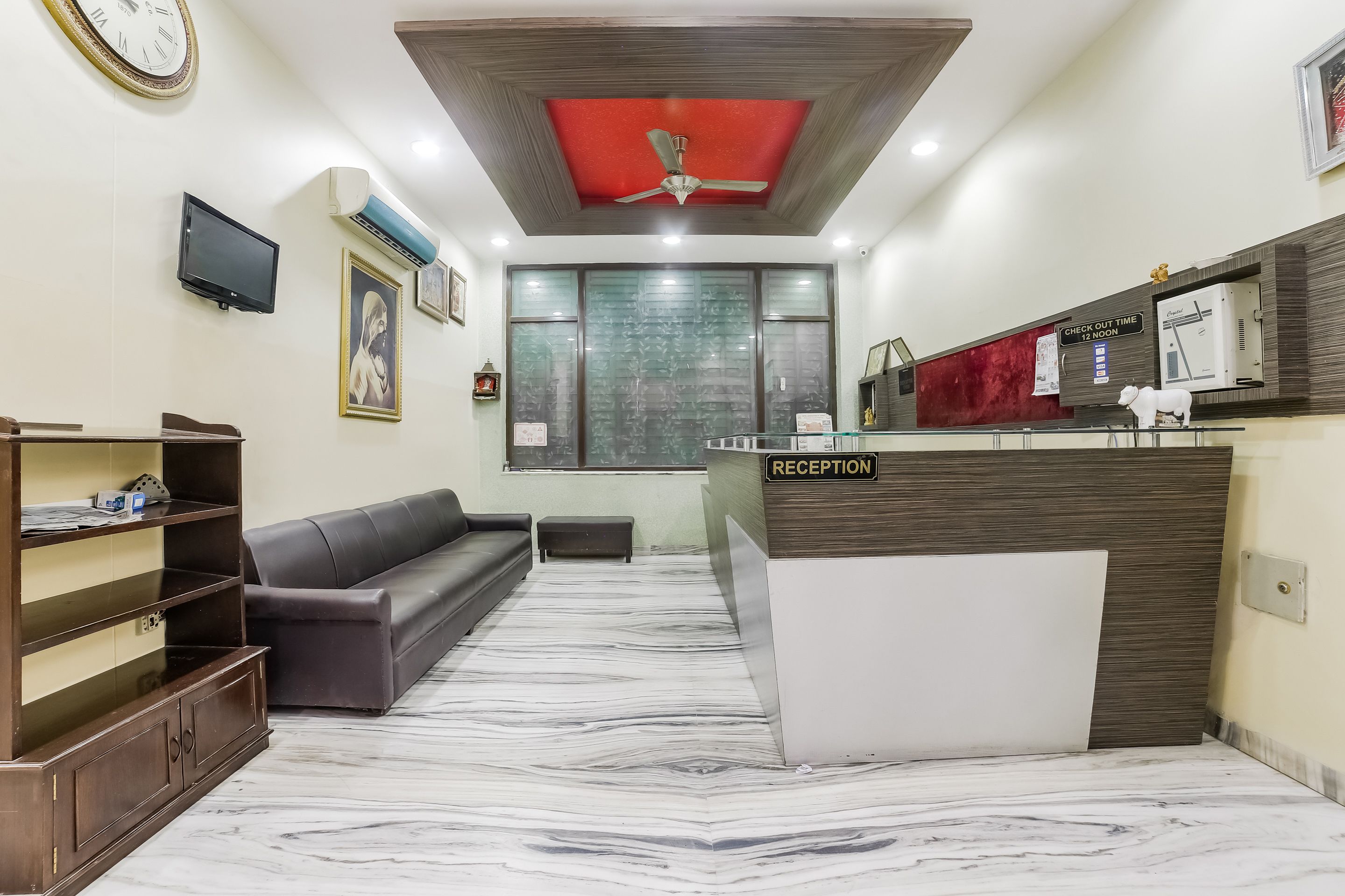 A reception area with a marble floor, a reception desk, a sofa, a television, and a ceiling fan.