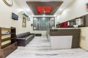 Un área de recepción con suelo de mármol, mostrador de recepción, un sofá, un televisor y un ventilador de techo.