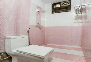 Un baño con paredes de azulejos rosa y blancos, un inodoro, una zona de ducha y una ventana con un adorno encima.