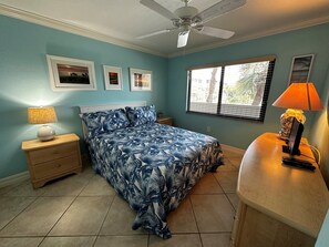 A bedroom with a bed, a nightstand, a desk, a ceiling fan, and a window with blinds.