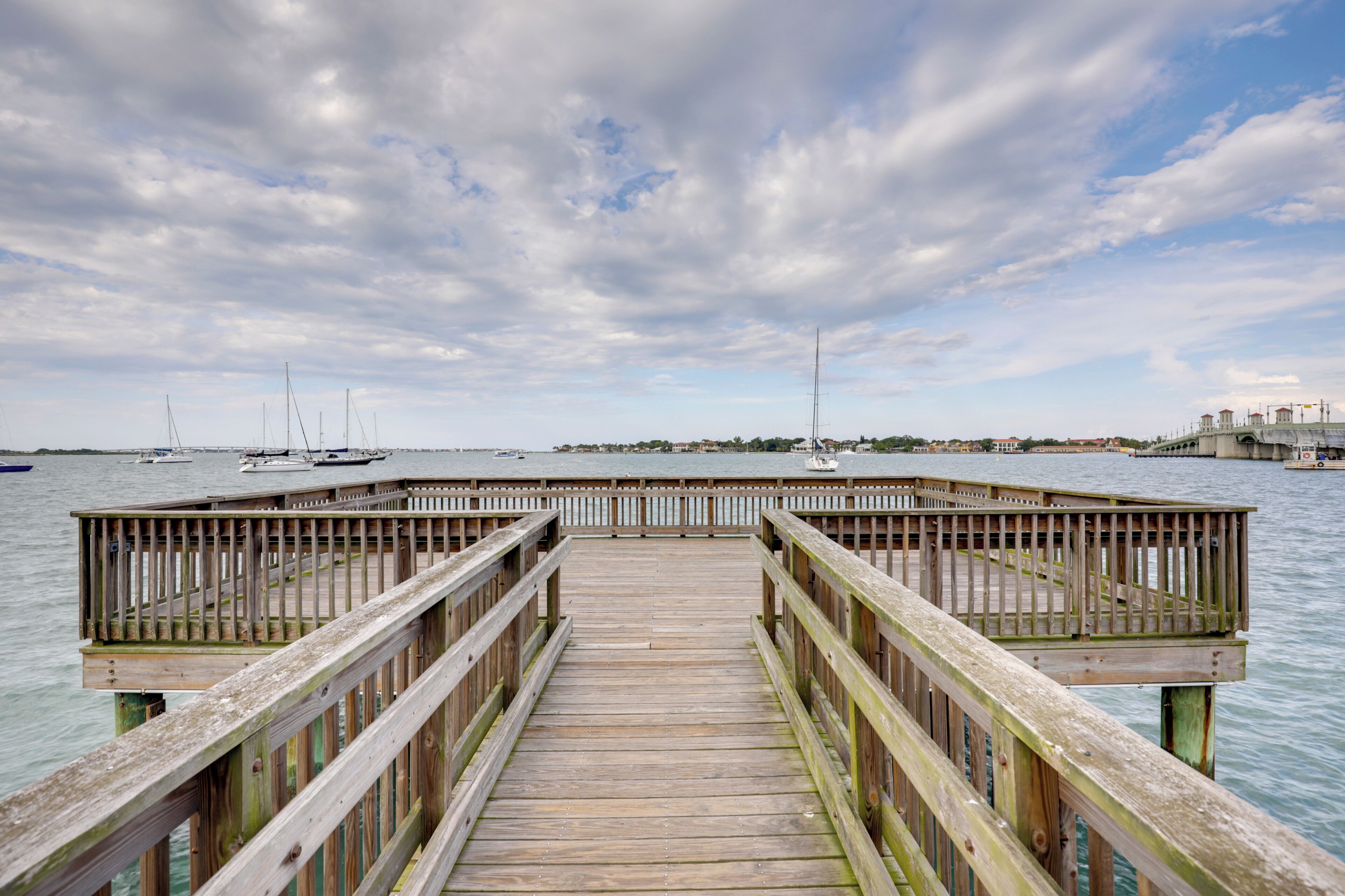 A wooden pier leading to a dock with boats in the background.