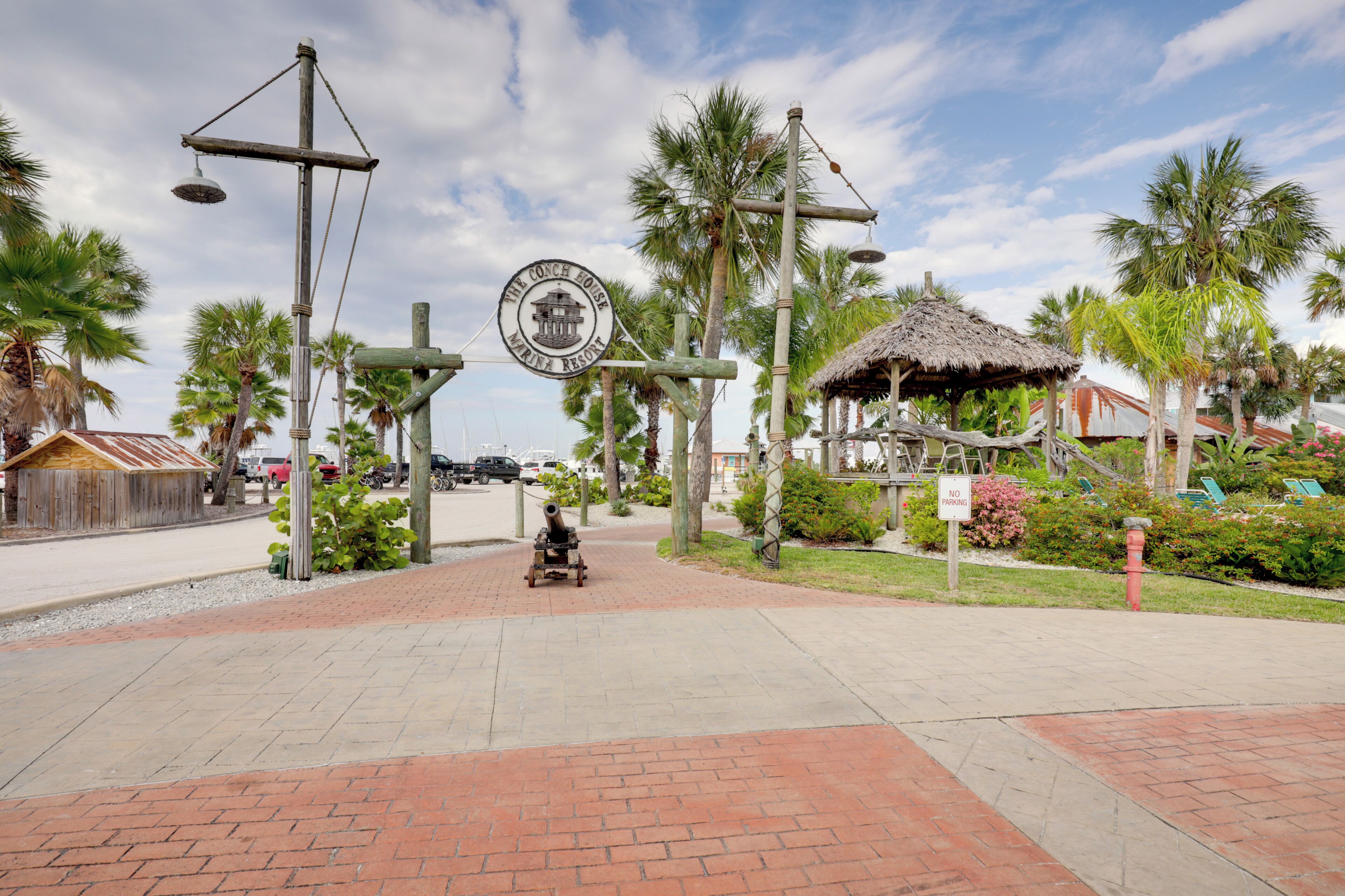 Une allée pavée, un panneau indiquant « The Conch House Marina Resort », des palmiers et une structure à toit de chaume.