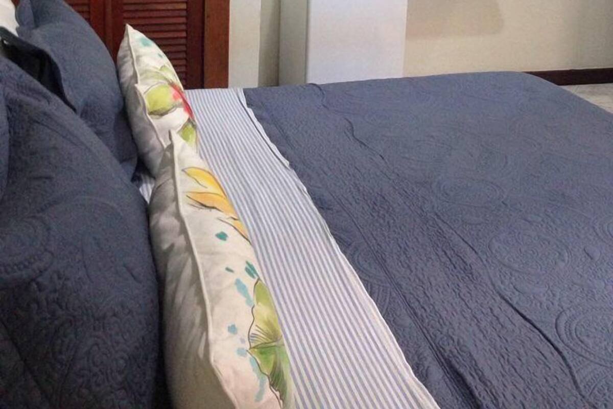 Makuuhuoneessa on sänky, puinen vaatekaappi ja pieni valkoinen pöytä, jonka yläpuolella seinällä on kaksi kehystettyä kuvaa.