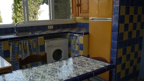 A kitchen with a washing machine, a table with a patterned tablecloth, and a window with curtains. - pretty house with wonderful sea view wifi available throughout the property (Spagna)