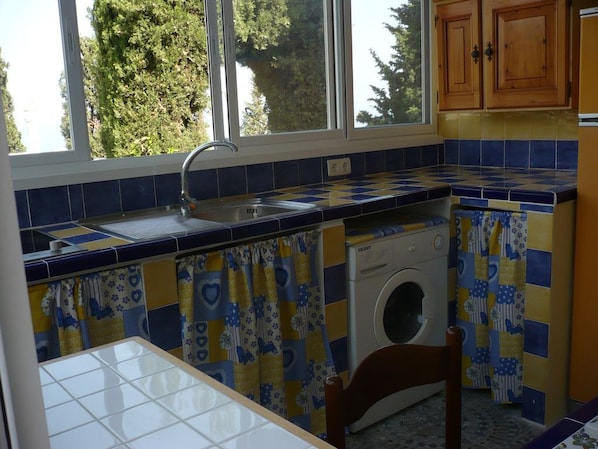 Une cuisine équipée d’un lave-linge, d’un évier et d’une fenêtre avec des rideaux.