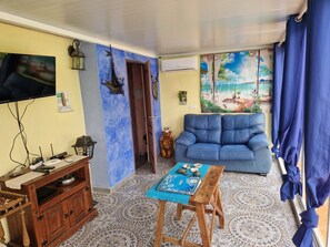 A living room with a blue sofa, a television, a wooden cabinet, and a tiled floor. - pretty house with wonderful sea view wifi available throughout the property (Spagna)