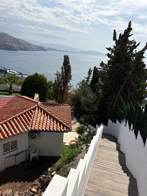 A residential property with a red-tiled roof, a staircase leading to a white-walled building, and a view of a body of water and distant mountains.