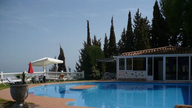 A swimming pool with a sunshade, lounge chairs, and a building with large windows. - pretty house with wonderful sea view wifi available throughout the property (Spagna)