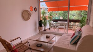 A modern living room with a white sofa, a wicker chair, a glass coffee table, and a view of an outdoor patio with a table and chairs. - renovated beach apartment  (Playa de las Americas - Arona)