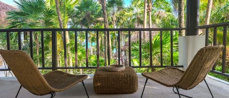 Ein Balkon mit zwei Korbstühlen und einem gewobenen Hocker, mit Blick auf einen Pool und Palmen.