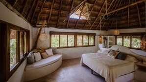 A room with a thatched roof, a bed, a curved seating area, and large windows. - Casa Mandala (Tulum)