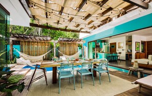 A modern outdoor dining area with a pool, bamboo decor, and a view of the kitchen. - Villa Amalfi (Tulum)