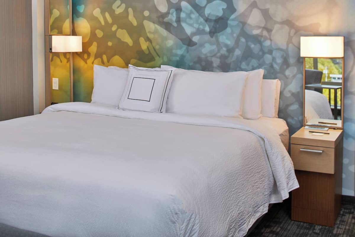 Una habitación de hotel con una cama grande, dos lámparas de noche, una mesita de noche con lámpara y un espejo.