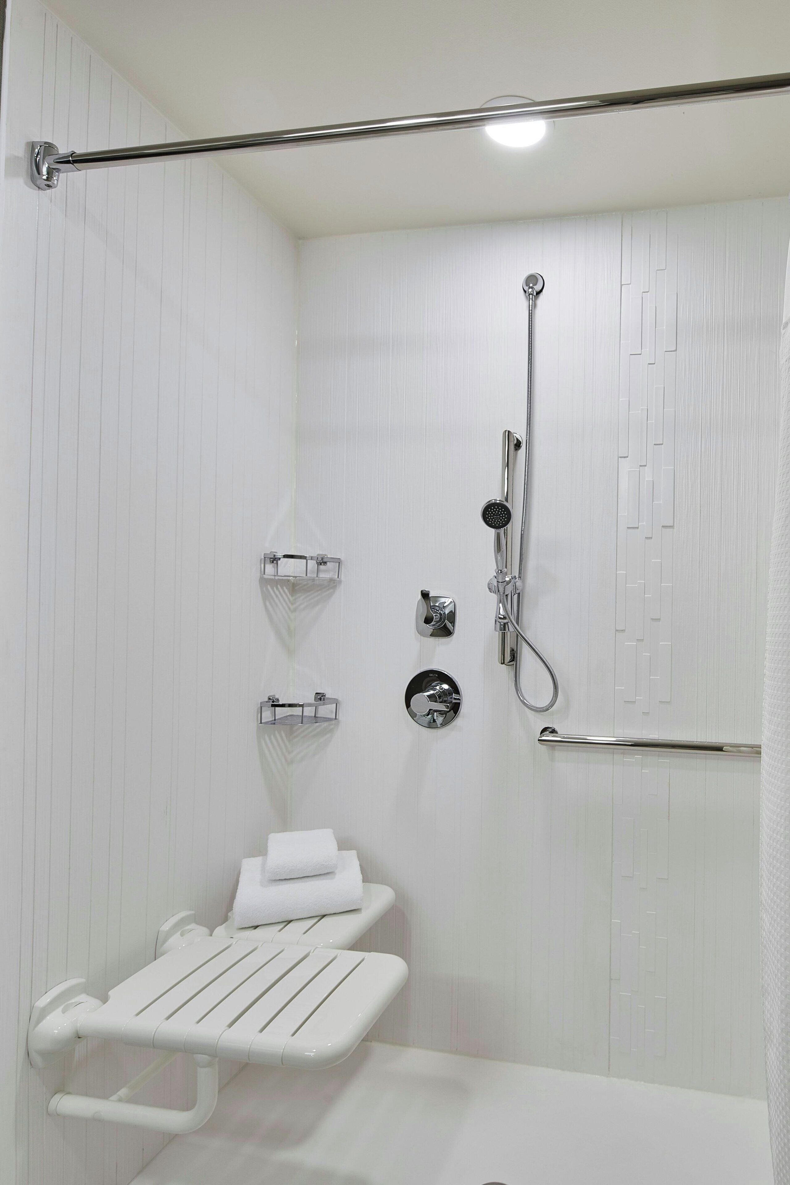 A small, white, walk-in shower with a handheld showerhead, a handheld showerhead, a towel rack, and a towel shelf.