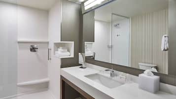 Un baño moderno con un espejo grande, lavamanos blanco y zona de ducha.