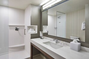 A modern bathroom with a large mirror, white sink, and a shower area. - Courtyard by Marriott Albany Airport (Albany)