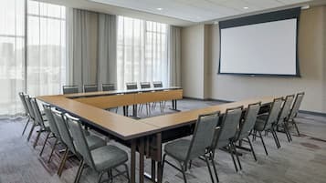 A conference room with a long table, chairs, a projector screen, and large windows with curtains.