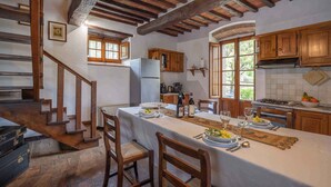 A rustic dining area with a long table set for a meal, wooden chairs, and a staircase leading to an upper level. - Holiday apartment with outdoor pool and WiFi (Cortona)