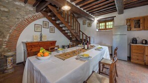 A dining area with a table set for a meal, a wooden staircase, and a kitchen area with cabinets and a refrigerator. - Holiday apartment with outdoor pool and WiFi (Cortona)