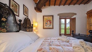 A bedroom with a large bed, a wooden headboard, a painting on the wall, and a window with a view of greenery. - Holiday apartment with outdoor pool and WiFi (Cortona)