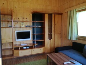 Ett rum med träpanel på väggarna, en tv som är monterad på en hylla, en soffa och ett soffbord.