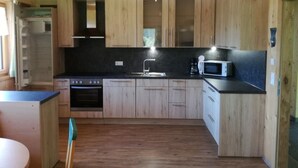 A compact kitchen with wooden cabinets, a black countertop, a stove, a microwave, and a sink. - FeWo Mooslechnerhof in a beautiful quiet location (Virgen)