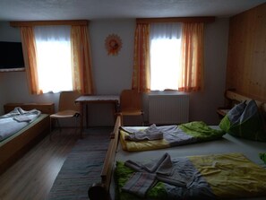Ett studentrum med en säng, ett skrivbord, två stolar, ett element och gardiner.