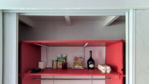 Una pequeña kitchenette con encimera roja, que contiene una botella de vino, un cartón de leche, una bolsa de pan y un cartón de huevos.