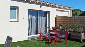 Un patio con mesa y sillas, un cerramiento de vidrio corredero y una valla de madera con plantas.