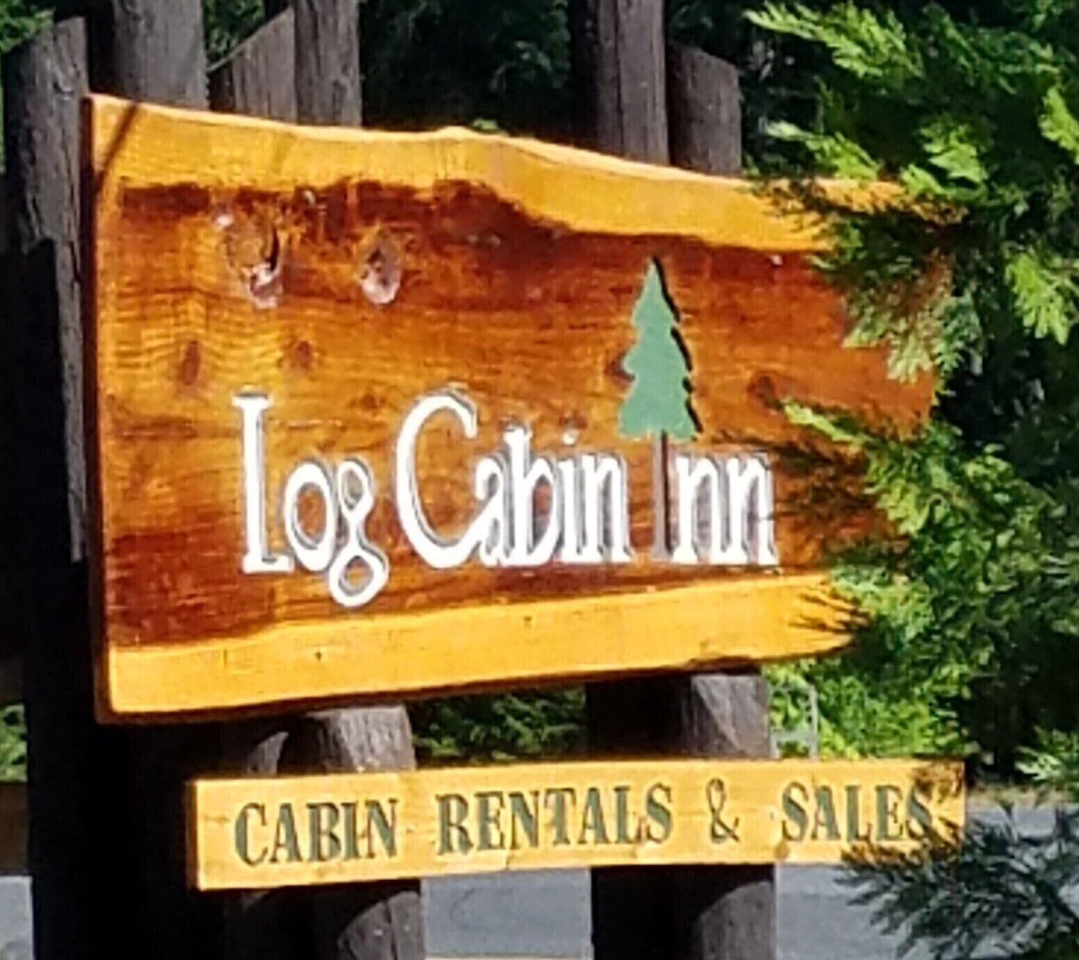 Een houten bordje voor Log Cabin Inn met de tekst 'CABIN RENTALS & SALES'.